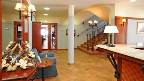 A hotel lobby with a reception desk, a staircase, and a seating area.