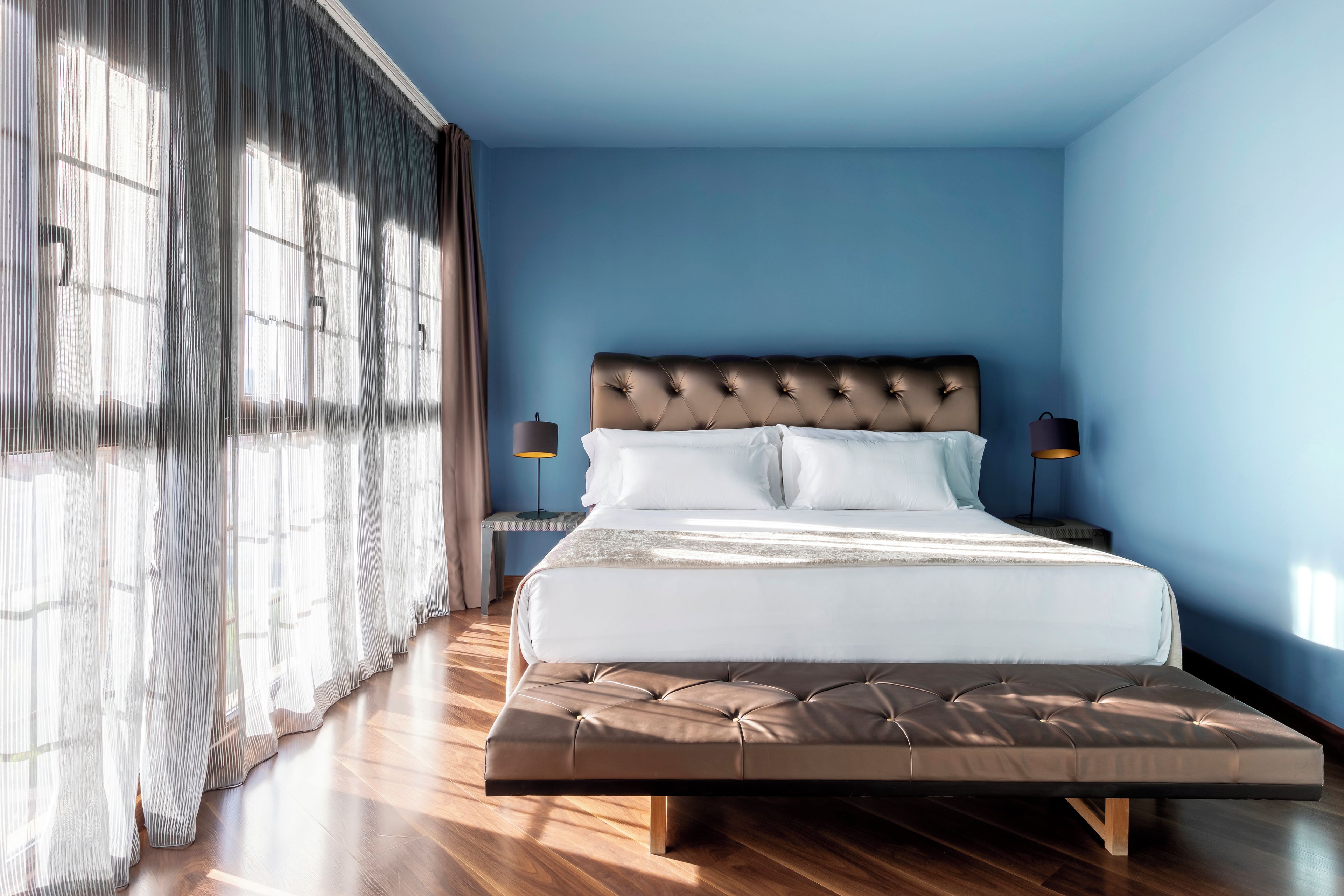 Une chambre à coucher avec un lit, deux lampes de chevet, une fenêtre avec des rideaux et un plancher en bois.