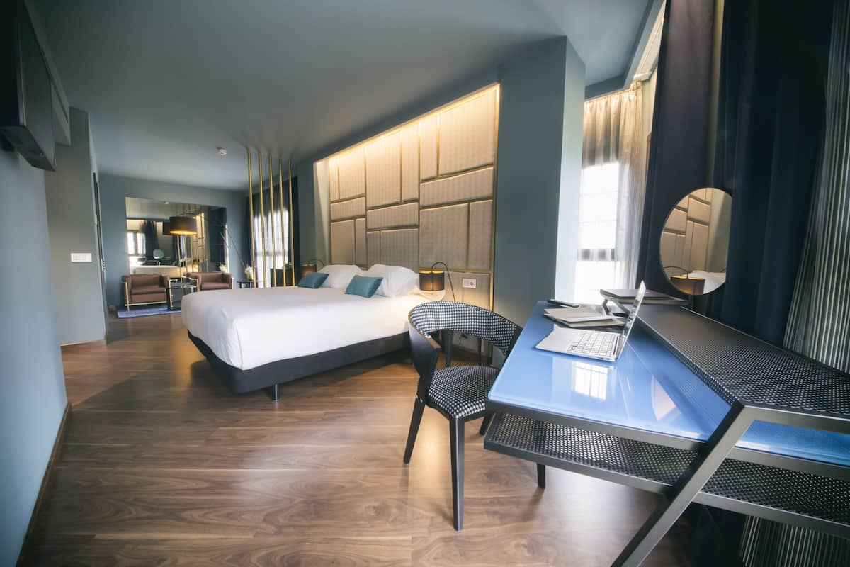 Una habitación de hotel moderna con una cama grande, un escritorio con silla, un espejo y vistas a la ciudad.