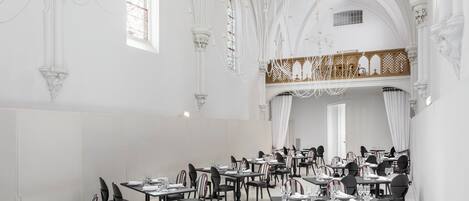 Un comedor espacioso con techos altos, candelabros y un balcón con barandilla de celosía.