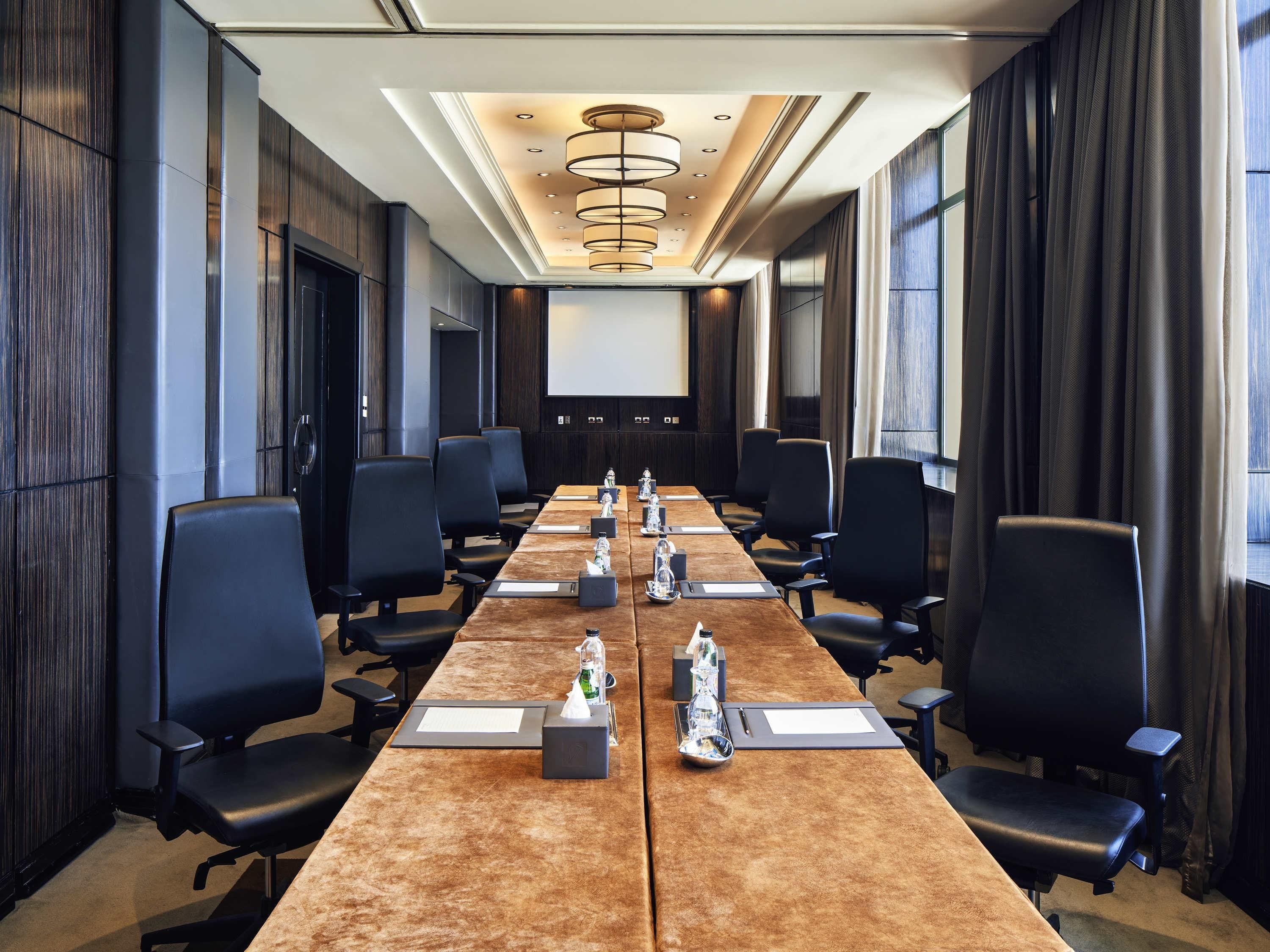A conference room with a long table, multiple chairs, and a projector screen.