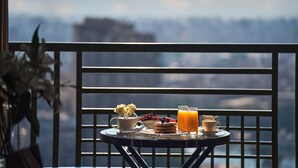 Un balcon avec une table préparée pour le petit-déjeuner, comprenant des crêpes, des fruits et du jus d’orange.