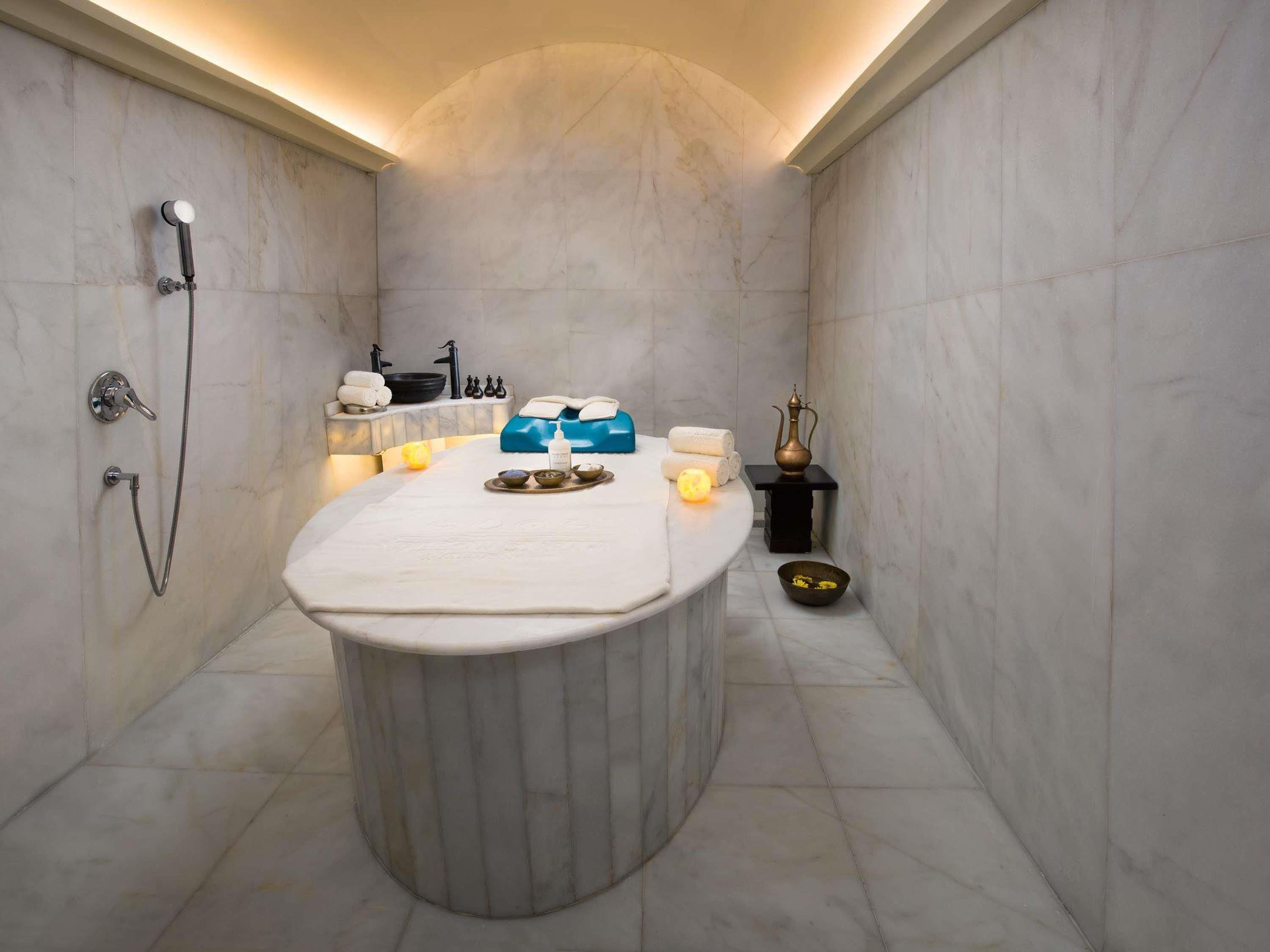 A spa room with a marble tub, a small table with toiletries, and a wall-mounted shower.