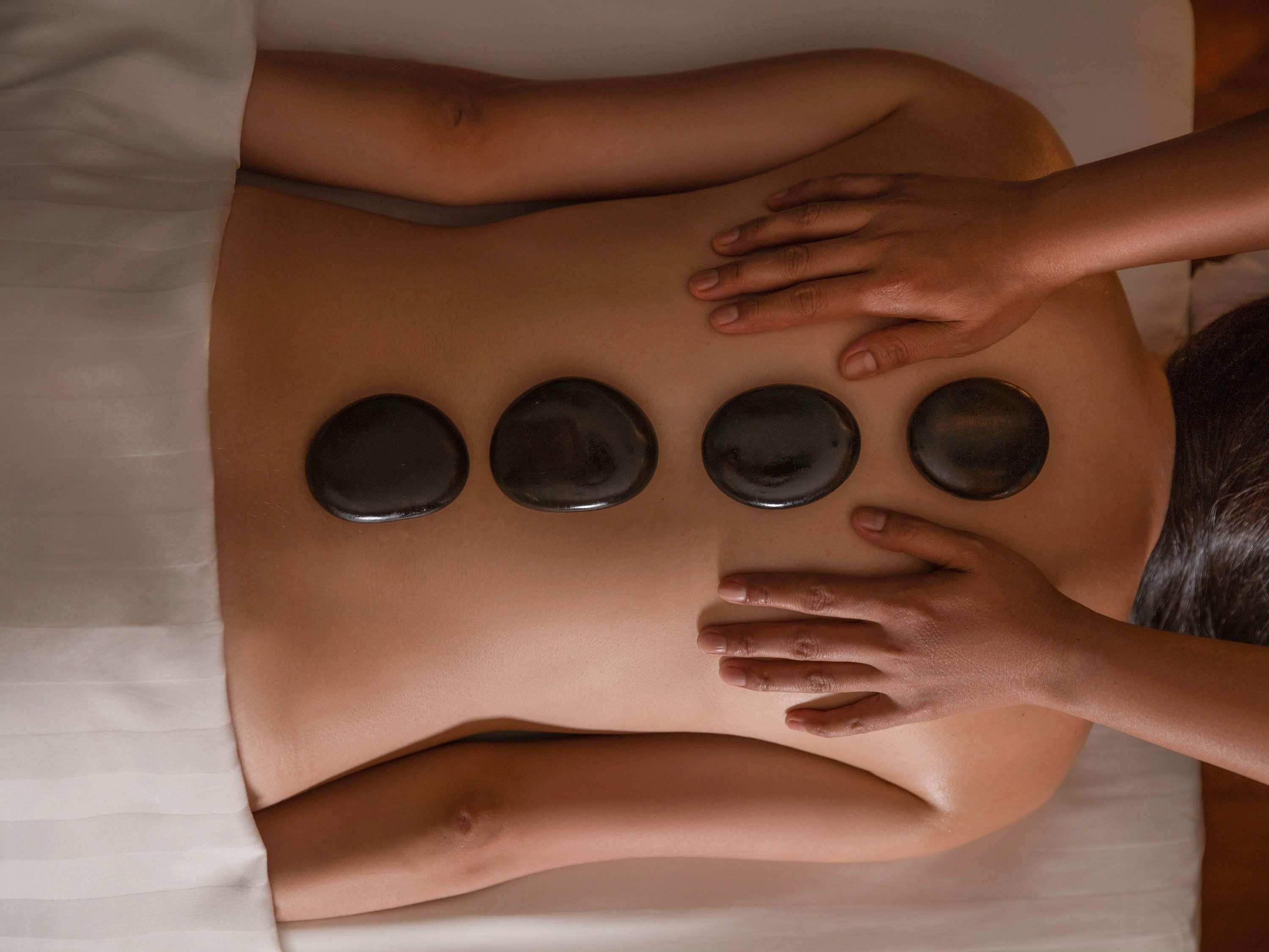 Una persona recibiendo un masaje en la espalda con cuatro piedras calientes colocadas sobre ella.