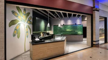 A modern reception desk with a wooden finish, a large decorative wall with a palm tree, and a green-tiled wall in the background.