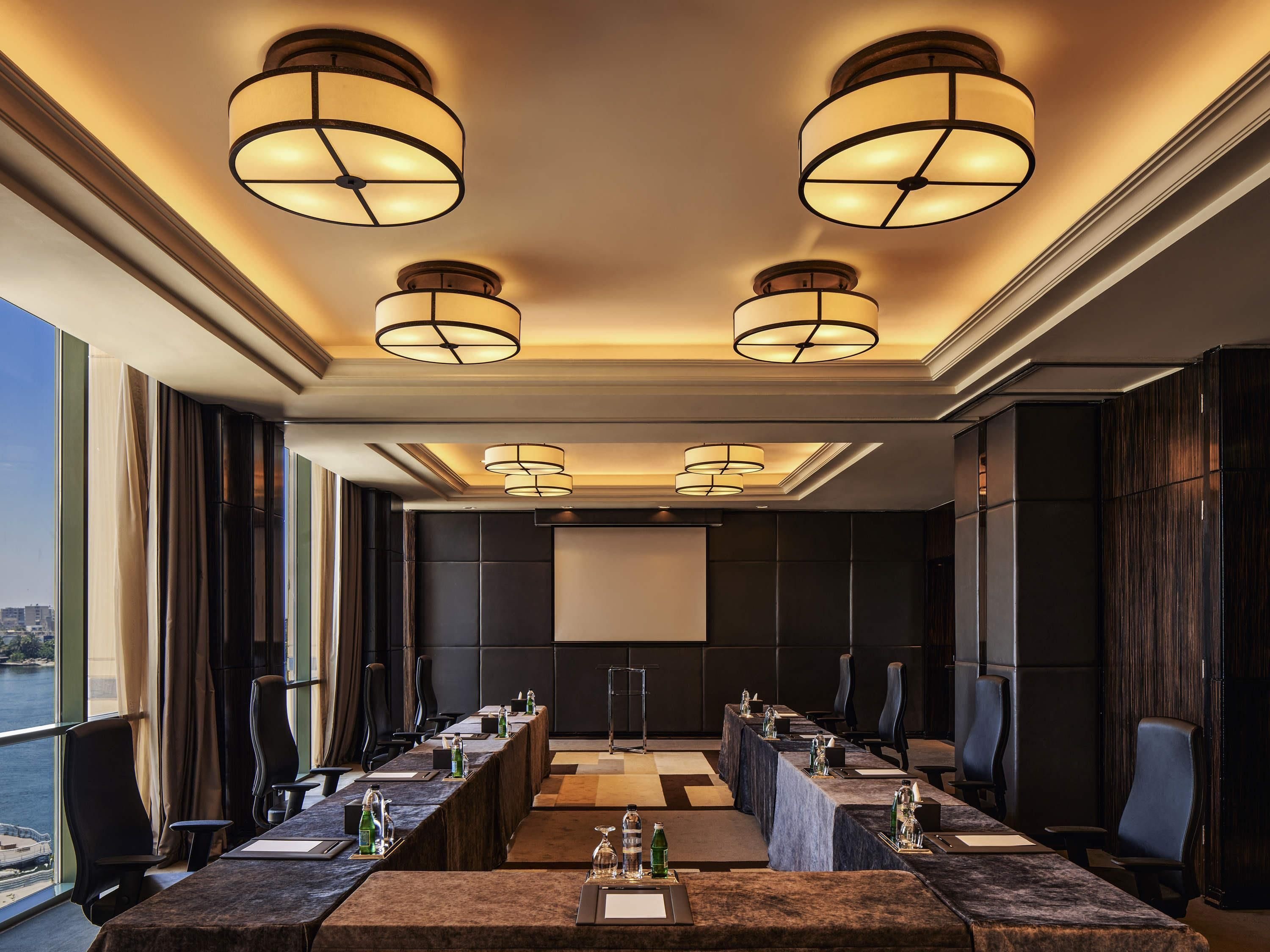 Un salón de conferencias con una mesa larga, varias sillas y tres luces en el techo.