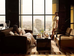 Una sala de estar moderna con un ventanal grande, un sofá, una mesa de centro con comida y vistas a la ciudad.