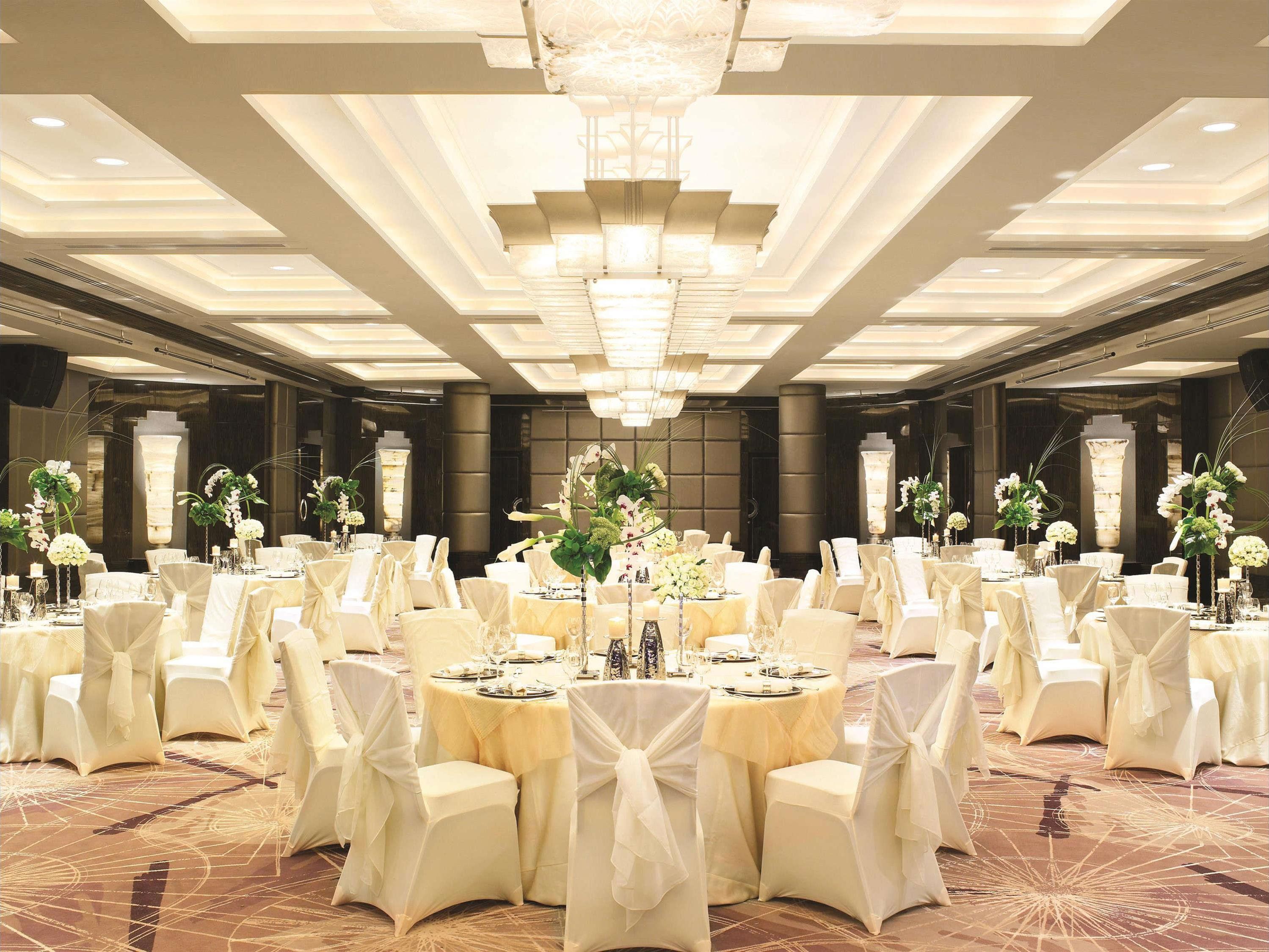 A banquet hall with round tables, white chairs, and floral centerpieces.