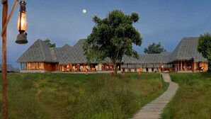 A series of thatched-roof buildings with a central tree and a pathway leading to them. - Evolve Back, Kabini (Heggadadevankote)