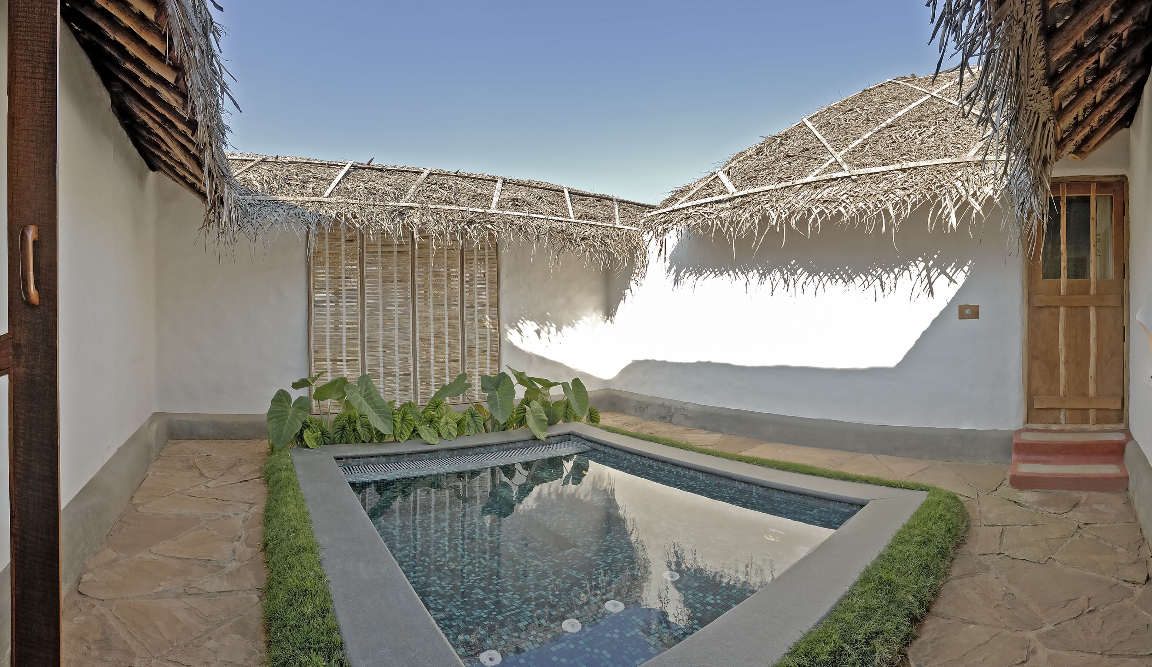A swimming pool with a tiled edge, surrounded by stone flooring and green grass.