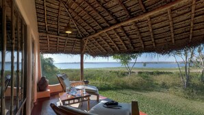 A covered outdoor seating area with a table and chairs, overlooking a body of water. - Evolve Back, Kabini (Heggadadevankote)