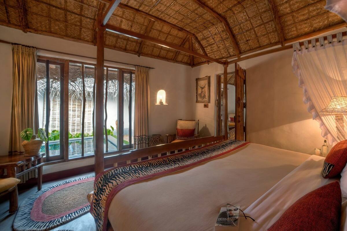 Ein geräumiges Schlafzimmer mit einem großen Bett, einer Holzbalkendecke und Blick ins Freie durch große Fenster.