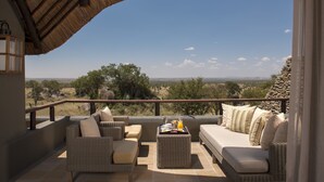 A balcony with wicker furniture, a tray with food, and a view of the savannah. - Four Seasons Safari Lodge Serengeti (Serengeti)