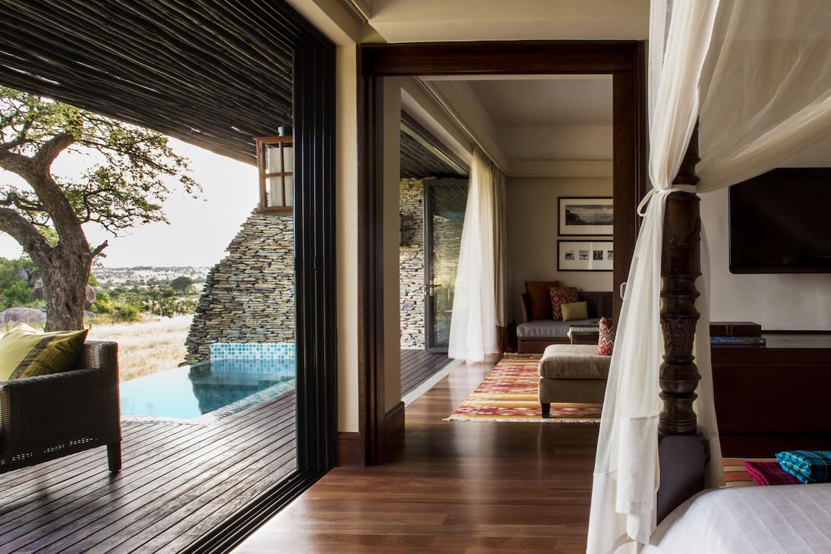 Ein Schlafzimmer mit großem Fenster, einem Bett, einem Fernseher und Blick auf Pool und Landschaft.