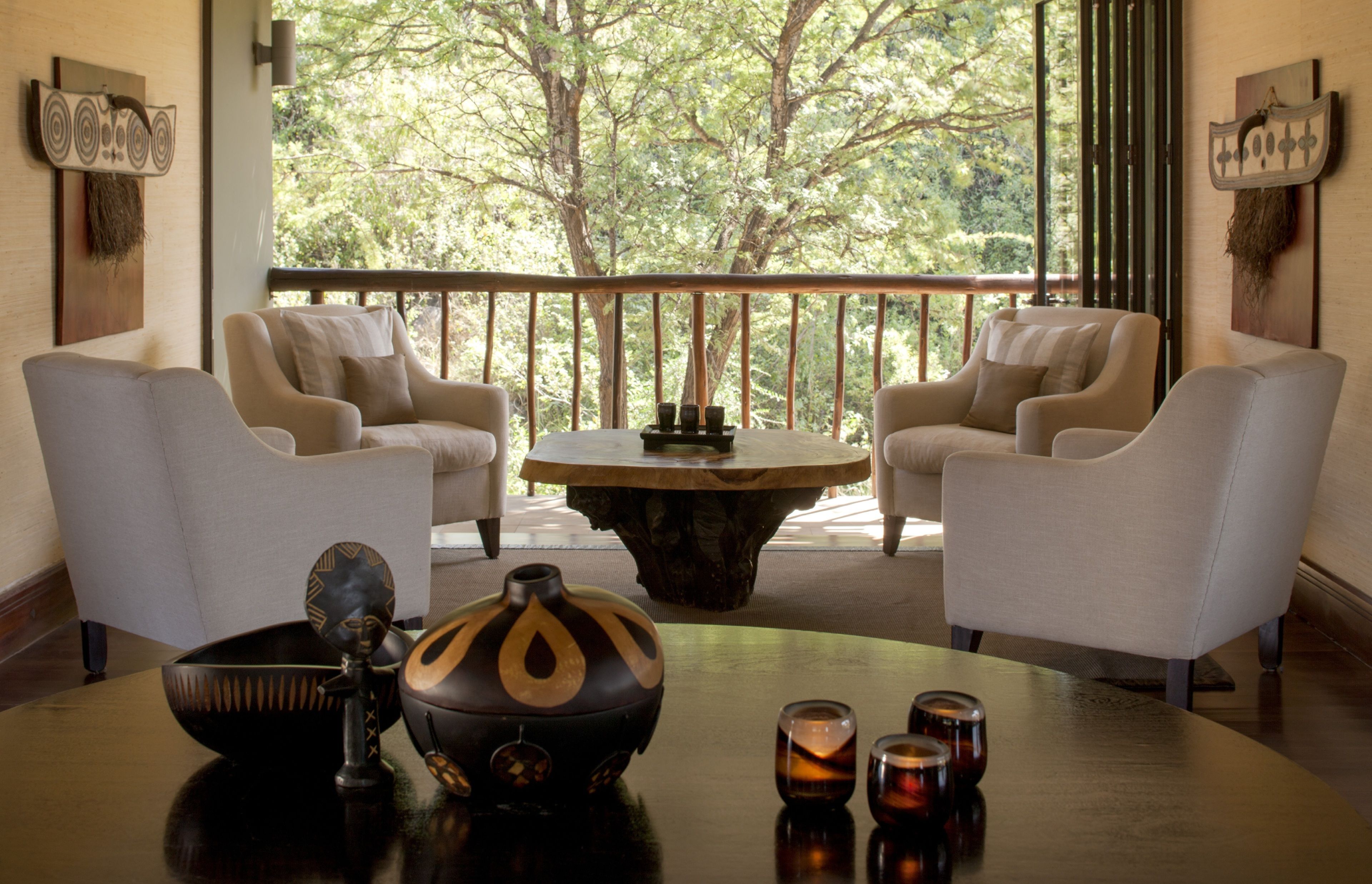A room with two armchairs, a round coffee table, and a view of trees through a balcony.