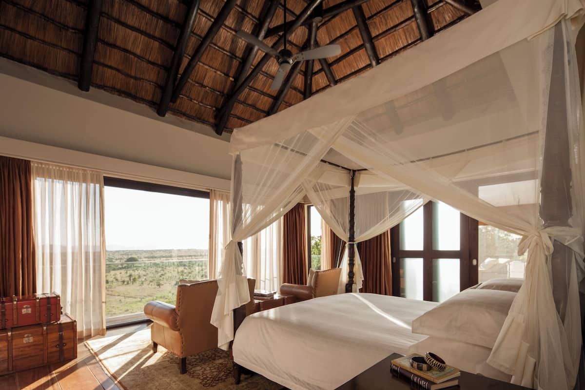 Ein Schlafzimmer mit Bett, Stuhl, Tisch mit Büchern, Koffer und Blick auf die Landschaft.