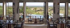 A dining area with tables and chairs, large windows offering a view of a natural landscape. - Four Seasons Safari Lodge Serengeti (Serengeti)