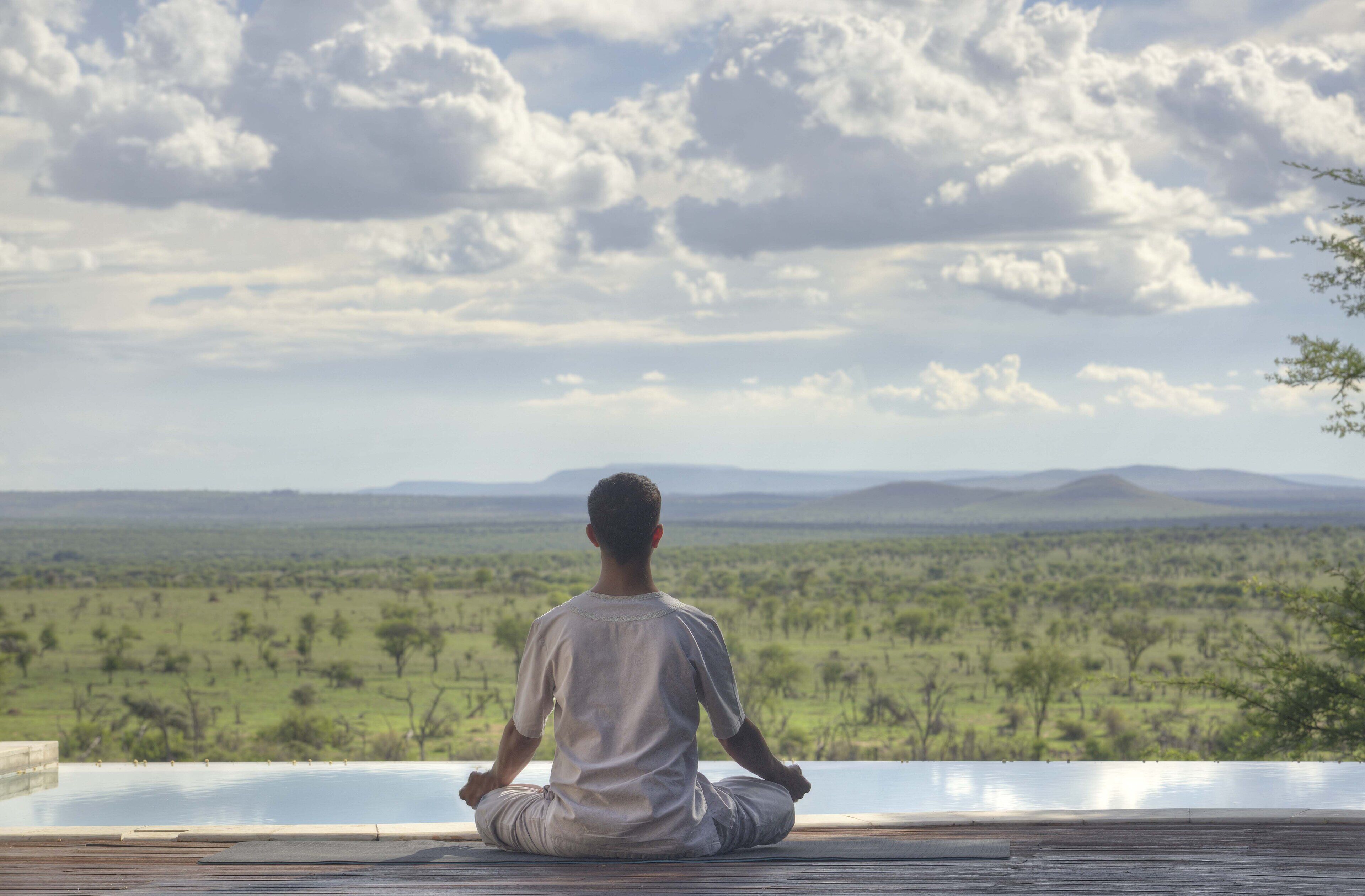 A person meditating on a wooden deck overlooking a savannah landscape.