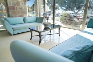 A modern living room with a light blue sofa, a glass coffee table, and a view of the outdoors through large windows.
