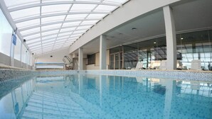 Una piscina interior con techo de cristal, agua cristalina y suelo de baldosas.