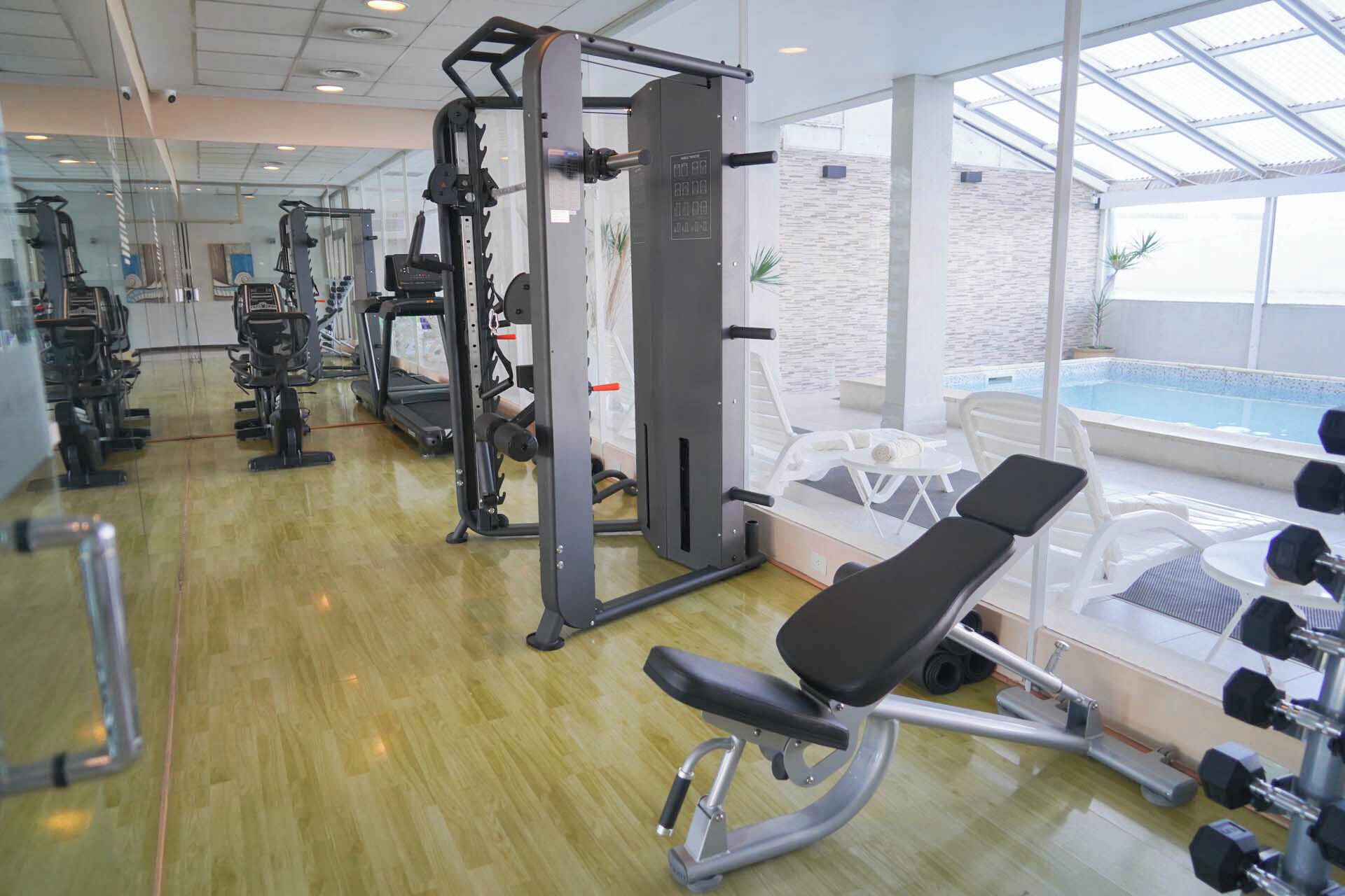 A gym with cardio machines, weightlifting equipment, and a bench.