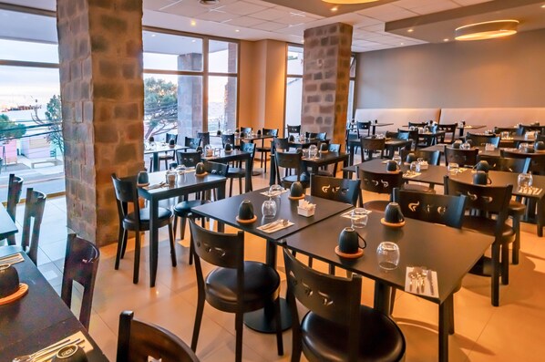 Un restaurante con varias mesas y sillas, ventanas amplias y pilares de piedra.