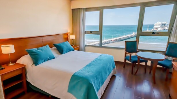 Habitación de hotel con una cama grande, un escritorio con silla y vistas al océano y al muelle.