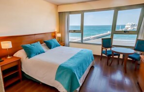 A hotel room with a large bed, a desk with a chair, and a view of the ocean and pier. - Yene Hue (Puerto Madryn)