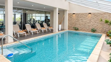 Een binnenzwembad met ligbedden en fitnessapparatuur.
