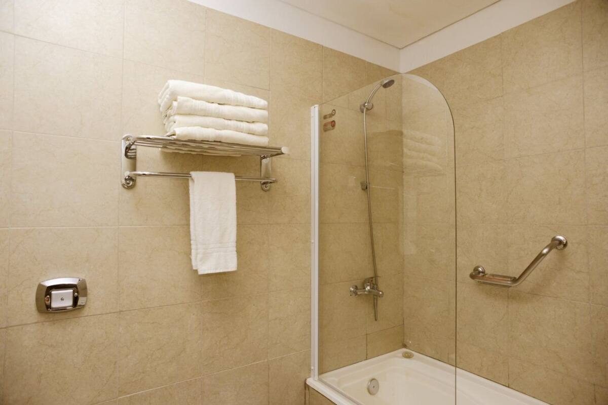 Une douche avec une porte en verre, un porte-serviettes avec des serviettes pliées et une barre d’appui.