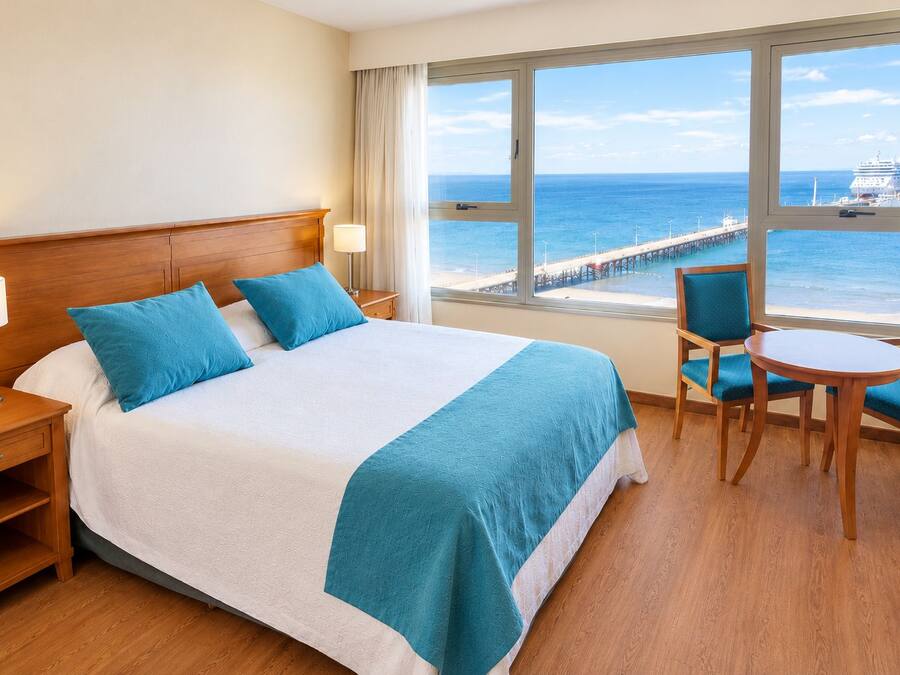 A hotel room with a large bed, a desk with a chair, and a view of the ocean.