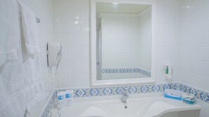 A bathroom with white tiles, a sink, a mirror, a towel rack, and a hand dryer. - Travelodge Bracknell (Bracknell)