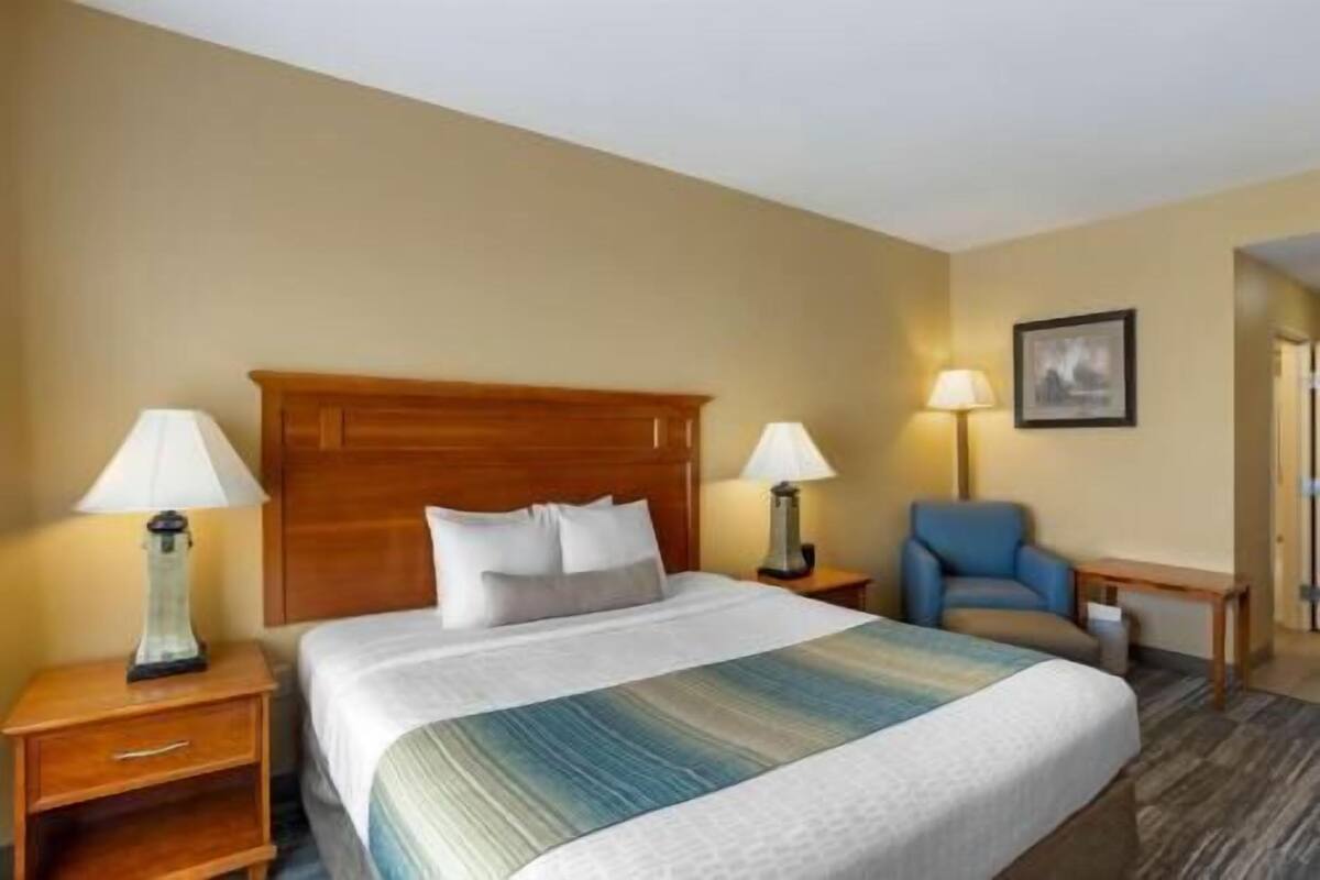 A hotel room with a large bed, two bedside tables with lamps, a blue armchair, and a framed picture on the wall.