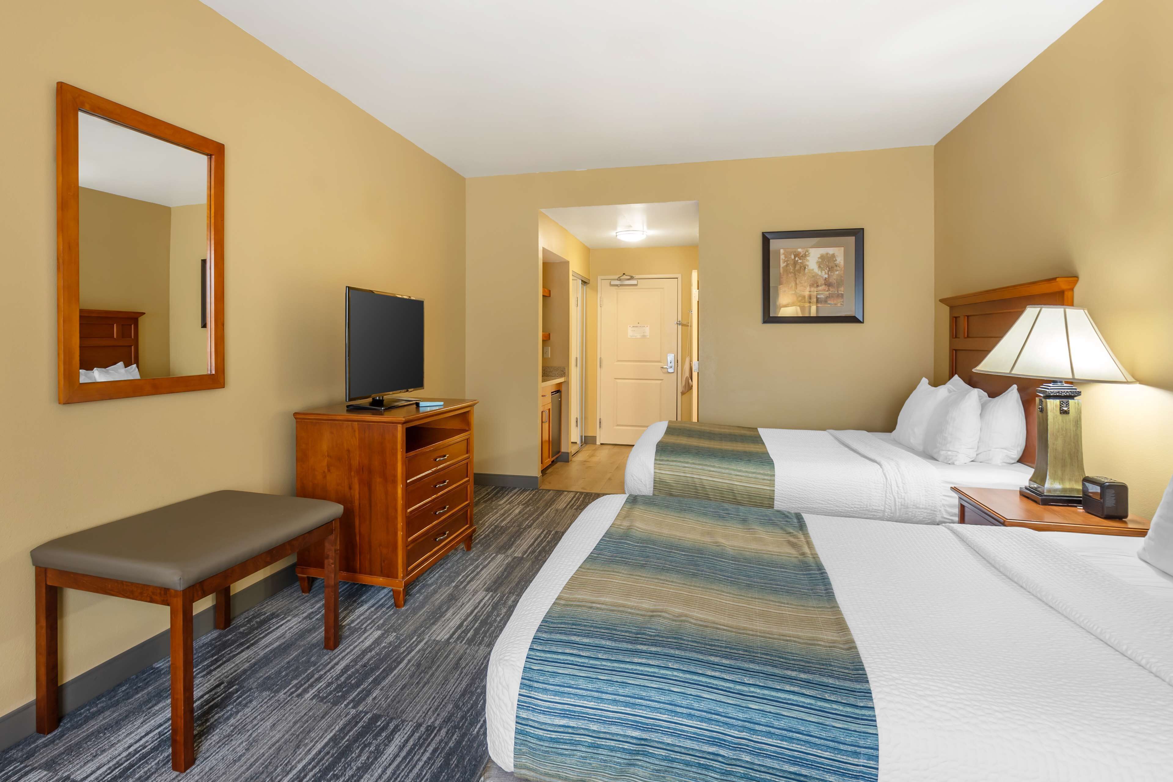 Una habitación de hotel con cama, escritorio, silla, televisor, lámpara y una puerta que da a otra habitación.