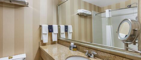 A hotel bathroom with a large sink, a mirror, and multiple towels on the wall.