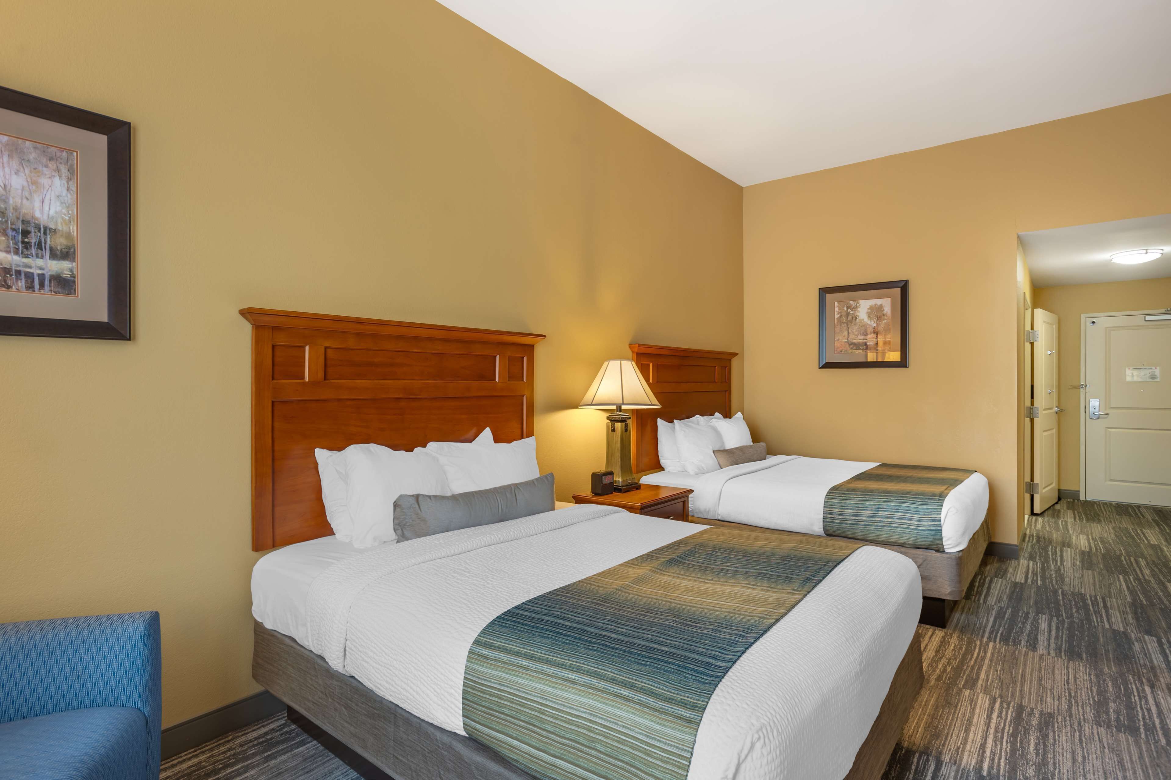 A hotel room with two beds, a wooden headboard, a nightstand with a lamp, and a framed picture on the wall.