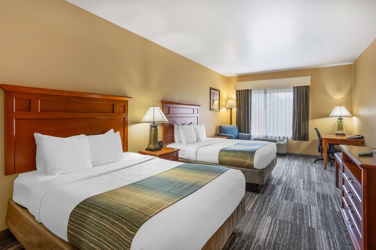 A hotel room with two beds, a desk, a chair, and a window with curtains.