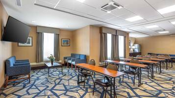 Une salle de conférence équipée de tables, de chaises, d’un téléviseur à écran plat et d’un tapis à motifs.