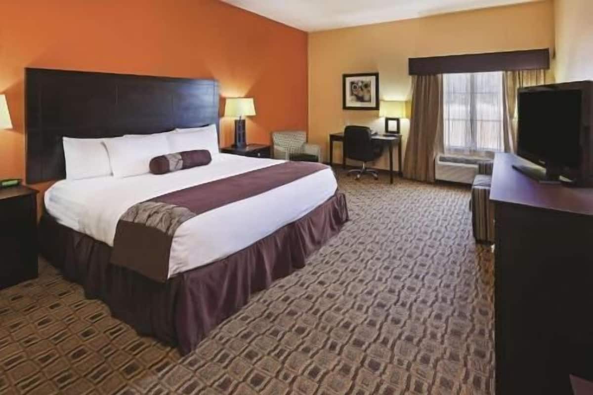 A hotel room with a large bed, a desk, a chair, a television, and a window with curtains.