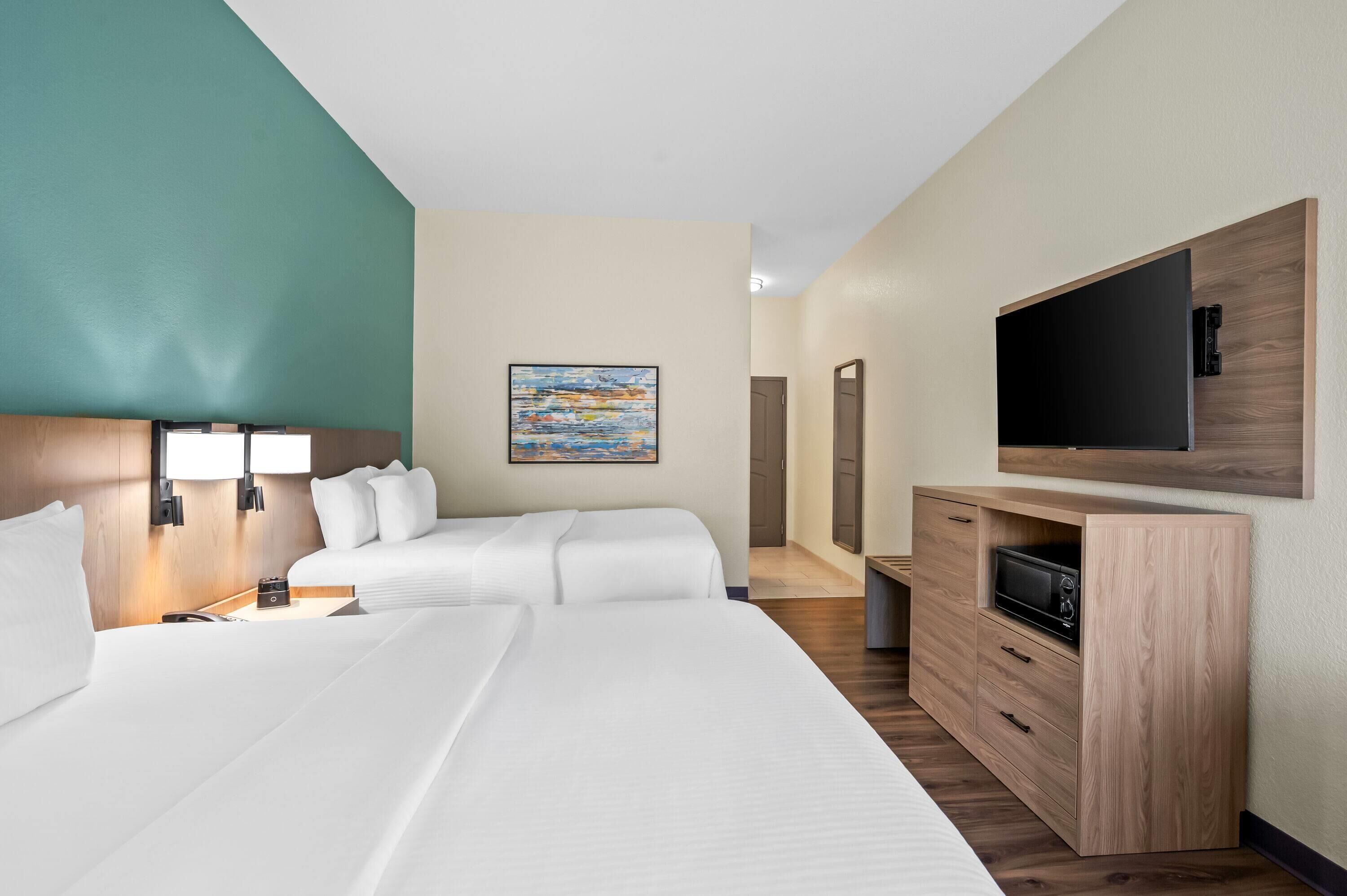 Ein Hotelzimmer mit zwei Betten, einem Fernseher, einem Gemälde und einem Schreibtisch mit Schubladen.