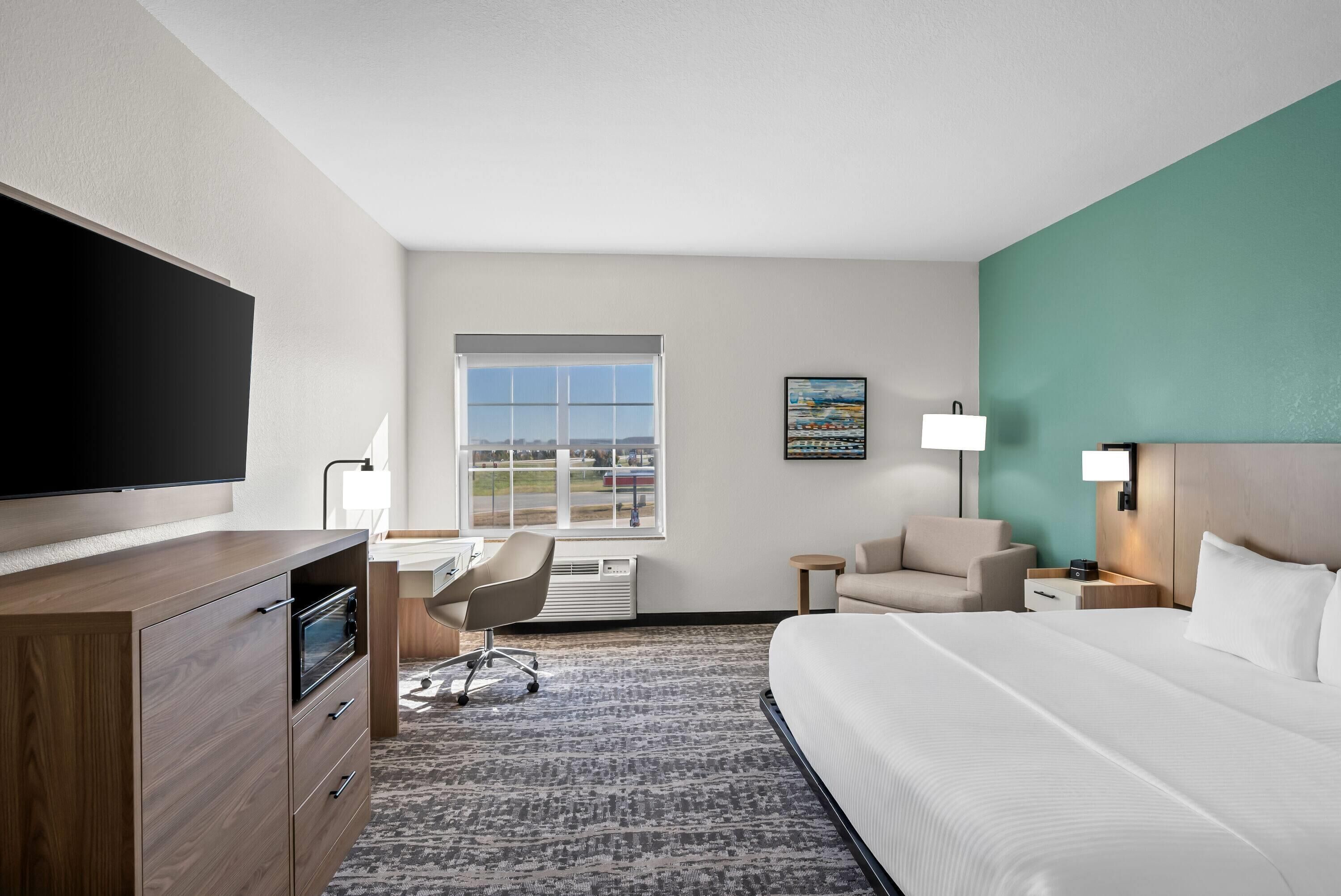 A hotel room with a bed, desk, chair, TV, and a window with a view.