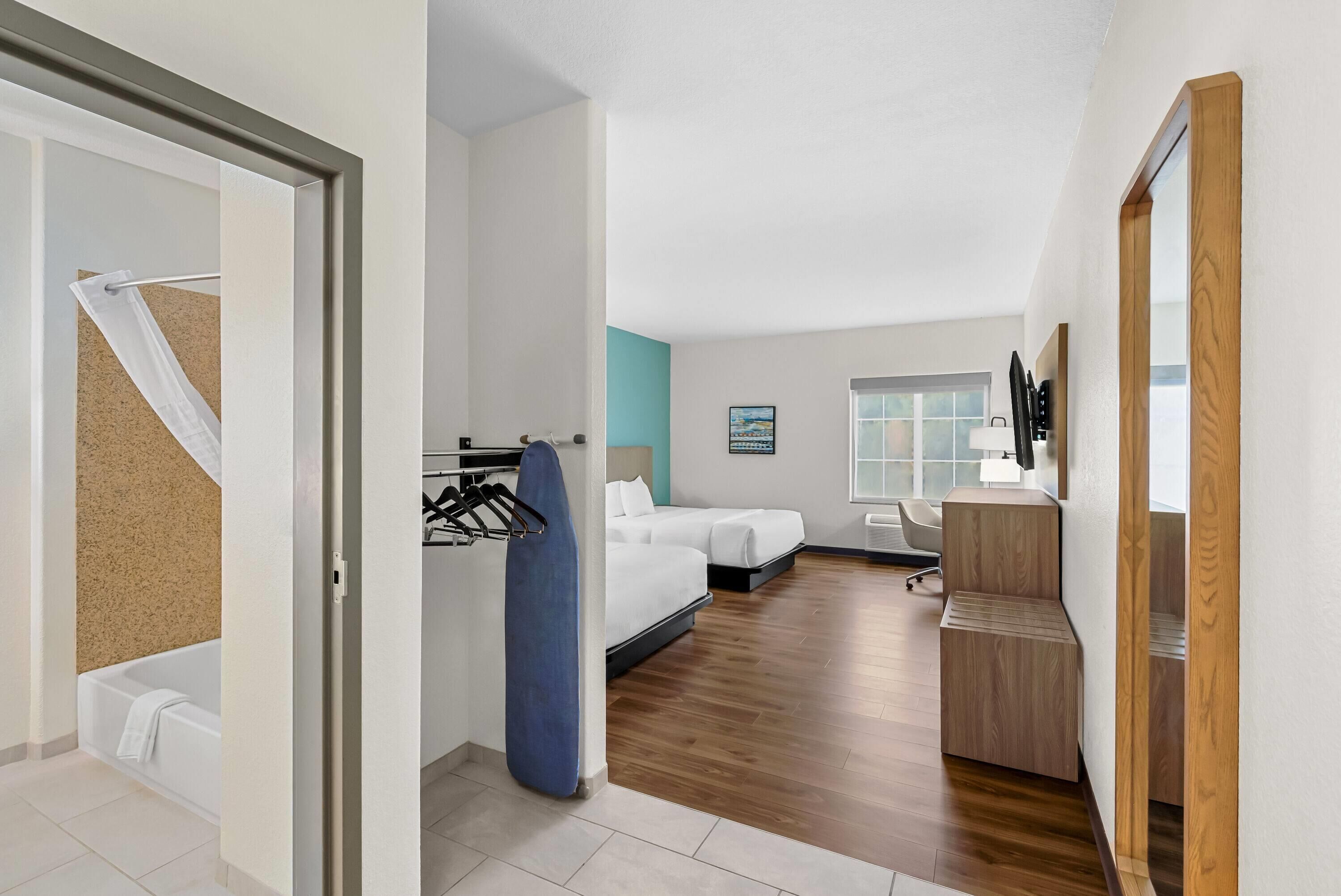 A modern hotel room with a wooden floor, a bed, a desk, and a bathroom with a bathtub and towel rack.