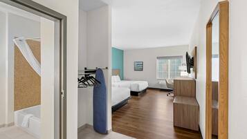 A modern hotel room with a wooden floor, a bed, a desk, and a bathroom with a bathtub and towel rack.