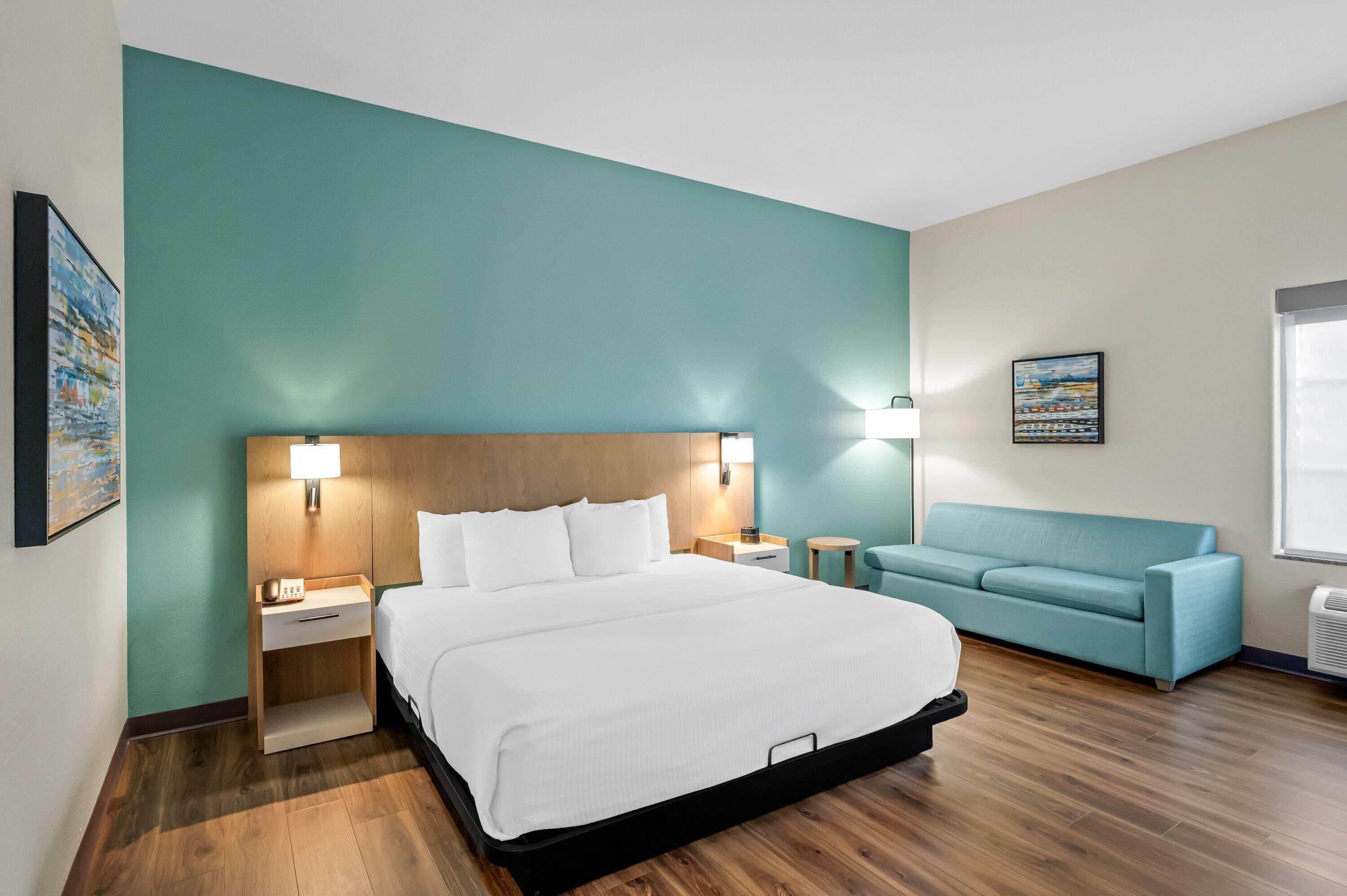 Une chambre d’hôtel avec un lit, une table de chevet, une lampe, un canapé et un tableau au mur.