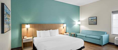 Une chambre d’hôtel avec un lit, une table de chevet, une lampe, un canapé et un tableau au mur.