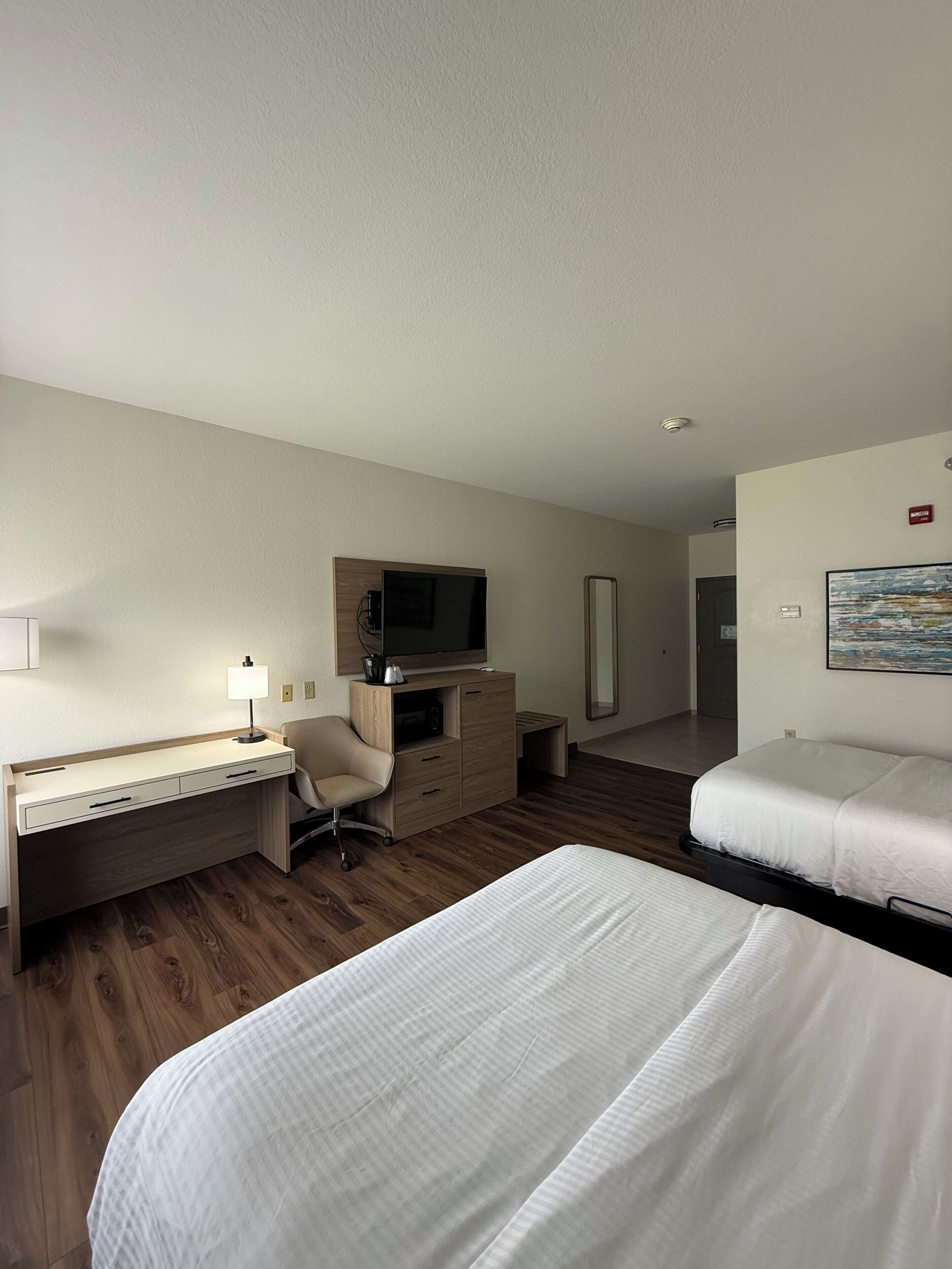Een hotelkamer met een bed, een bureau met stoel, een televisie, een dressoir en een schilderij aan de muur.
