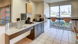 A modern kitchen with a large window, a coffee machine, and a sign encouraging saving money on travel. - Motel 6 Roanoke, TX - Northlake - Speedway (Roanoke)