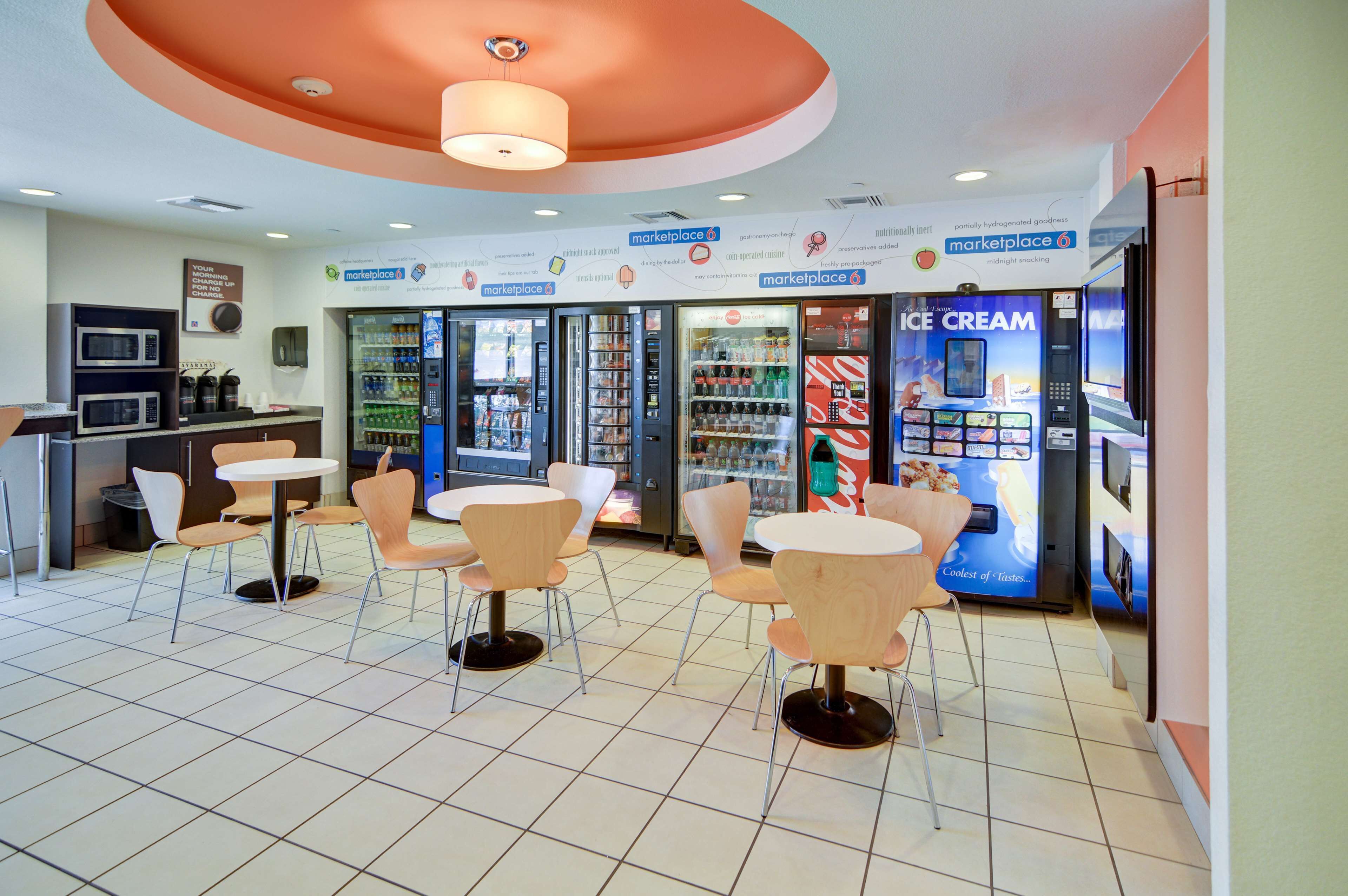 A modern indoor seating area with tables and chairs, vending machines, and a refrigerated display case.