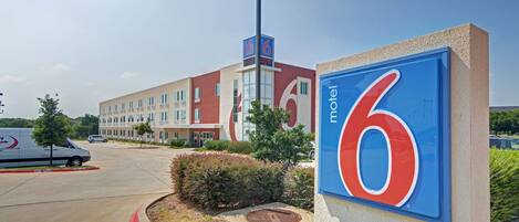 A motel sign with the number 6, a modern building with multiple windows, and a parking lot with a white van.
