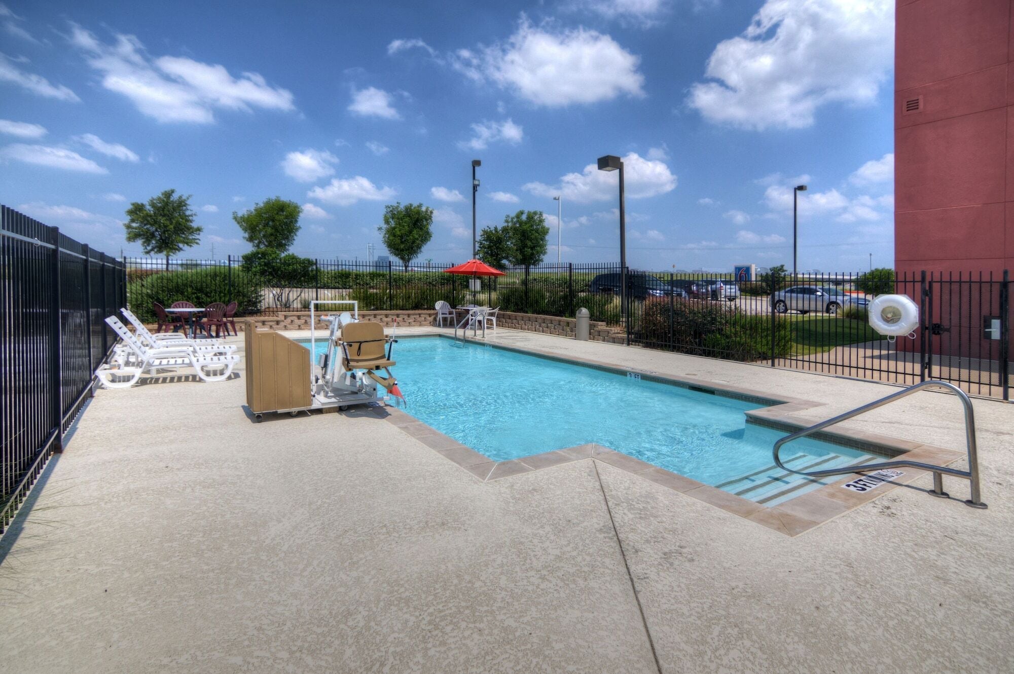 A swimming pool with a lifeguard chair, lounge chairs, and a red umbrella.